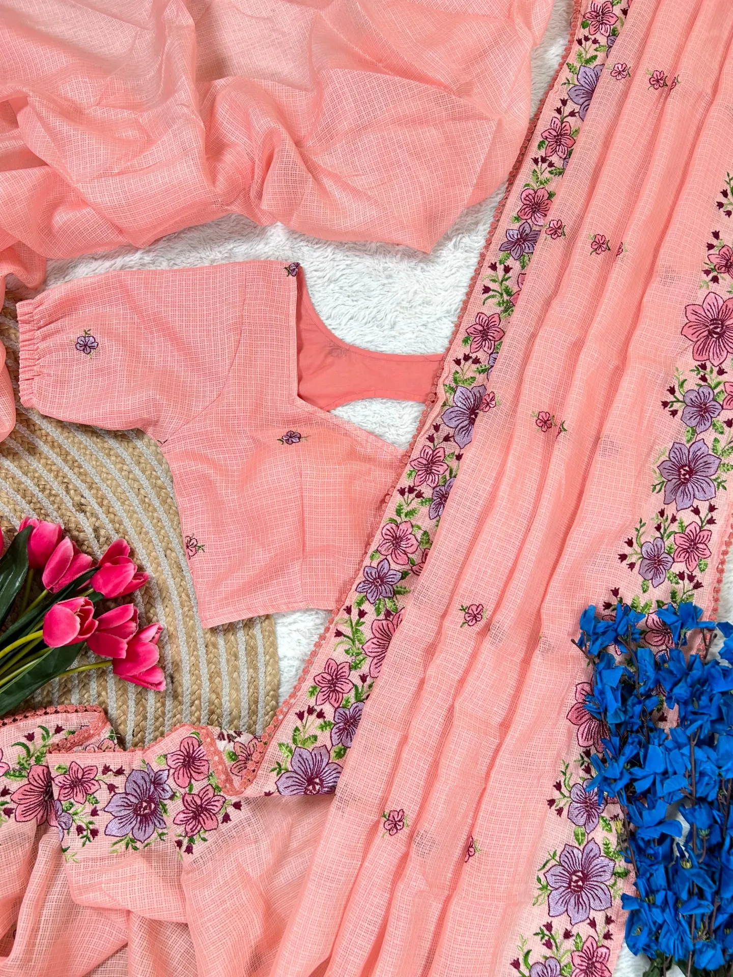 This ensemble features a lightweight, peach-colored sari crafted from a textured fabric, likely